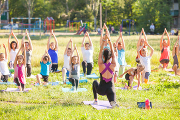 children do yoga with an outdoor trainer.