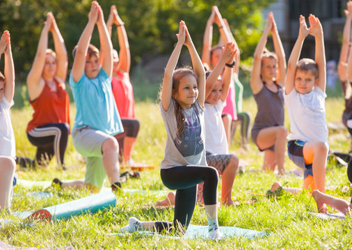 children do yoga with an outdoor trainer.