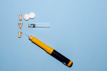 The abbreviation IVF is laid out in wooden letters on a blue background. In vitro injection pen,...