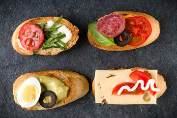 Open faced sandwich canape or crostini on dark stone background closeup. Top view.