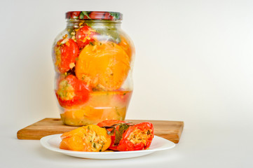 Stuffed vegetables pickled red and yellow peppers lie on a white plate on the background of a closed jar of peppers.