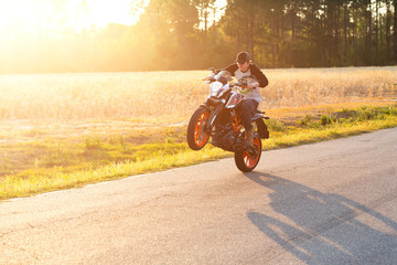 Teenage boy on a dirtbike motorcycle doing a wheelie at sunset - obrazy, fototapety, plakaty