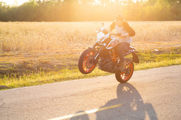 Teenage boy on a dirtbike motorcycle doing a wheelie at sunset