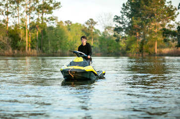 Teenage boy man driving a personal watercraft outside on a lake pond at sunset
