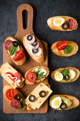 Open faced sandwich canape or crostini on a wooden serving board on dark stone  background closeup. Top view.