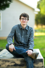 Obraz premium Teenage Boy with Glasses Outside on a spring day sitting outside of a house home smiling