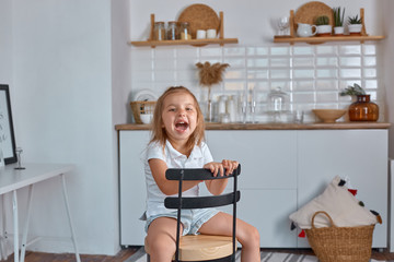 A smiling little girl sitting on the work surface of the kitchen waiting for breakfast. Cheerful and mischievous girl in the kitchen