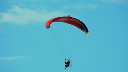 Red paraglider in flight. Paraglider flying against a clear blue sky.