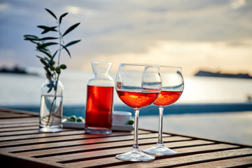 two glasses of rose wine with  olives against blue water on a pier..