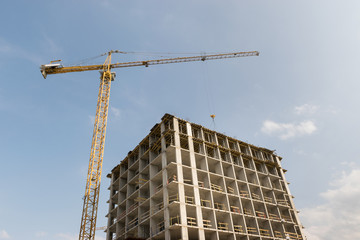 A high-rise construction crane against the sky is building a multi-storey building using modern technology from metal, concrete and brick, which will become an apartment building or office center