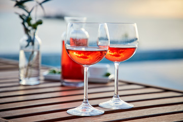 two glasses of rose wine with  olives against blue water on a pier..