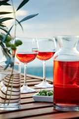 two glasses of rose wine with  olives against blue water on a pier..