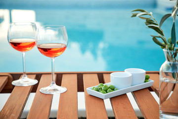 two glasses of rose wine with  olives against blue water on a pier..