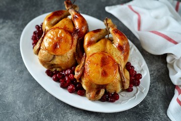 Two whole roasted chicken with cranberries and orange slices.