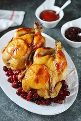 Two whole roasted chicken with cranberries and orange slices.