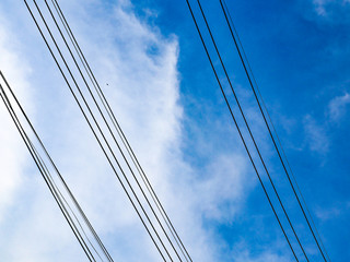Fototapeta premium Parallel power lines cross on the cloudy blue sky