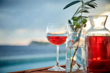 two glasses of rose wine with  olives against blue water on a pier..