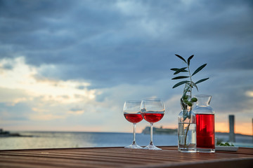 two glasses of rose wine with  olives against blue water on a pier..