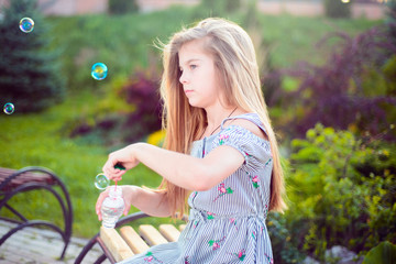 little teenage girl sitting on a bench blowing bubbles. Active lifestyle child