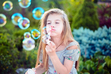 beautiful little girl, teenager, sitting on the bench, blows bubbles. Outdoors