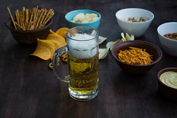 A glass of beer with pretzels and various snacks. Beer snacks. Wood background. View from above. Place for text.