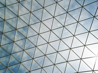 Glass roof with triangular cells and frames against the blue sky with white clouds. Reflections in glasses.
