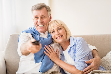 Loving mature couple watching tv with remote control