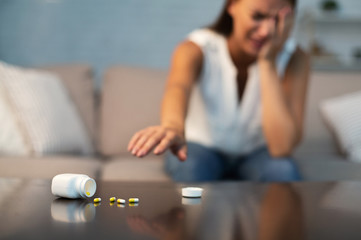 Suicidal Girl Reaching After Antidepressant Pills Sitting On Couch Indoor