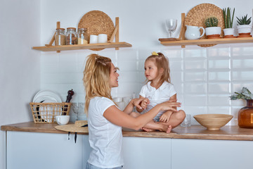 Little girl with mom smile and laugh. A girl sits on the working surface of the kitchen. A cheerful...