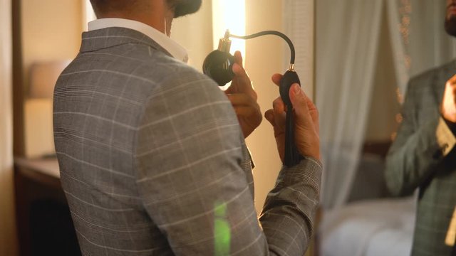 Young and handsome bearded man is using atomizer nozzle with perfume