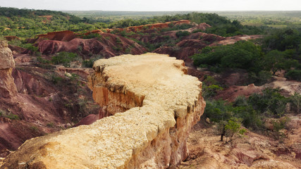 Photography of the Hell's Kitchen in Kenya: strip of yellow rock, in the background the valley with red ground and the forest with green trees.