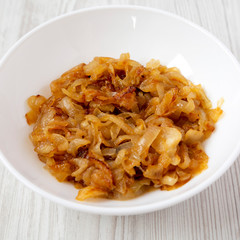 Homemade caramelized onions on a white plate on a white wooden surface, side view. Close-up.