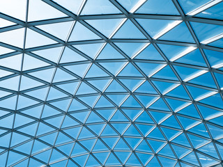 Glass roof with triangular cells and frames against the blue sky with white clouds. Reflections in the glass.