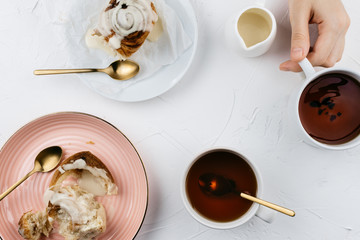 Flatlay of homemade cinnamon rolls with cream and tea on white cement background