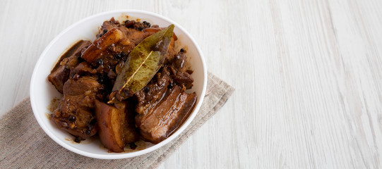 Homemade Filipino Adobo Pork in a bowl on a white wooden surface, low angle view. Space for text.