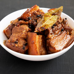 Homemade Filipino Adobo Pork in a white bowl on a black surface, side view. Close-up.