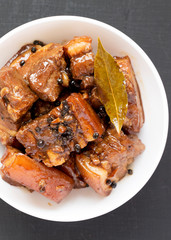 Homemade Filipino Adobo Pork in a white bowl on a black background, top view. Flat lay, overhead, from above. Close-up.
