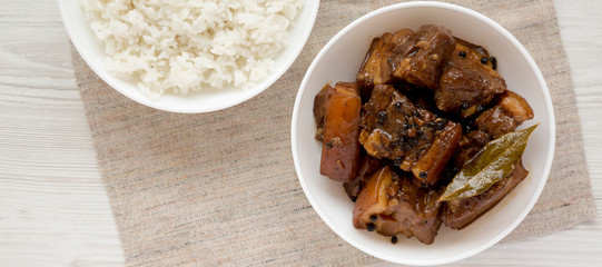 Homemade Filipino Adobo Pork with rice on a white wooden surface, top view. Flat lay, overhead, from above. Space for text.