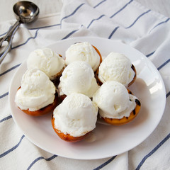Homemade grilled peaches with vanilla ice cream on a white plate, low angle view.