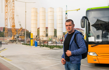 The young man with backpack is standing at the bus stop waiting for the trip near construction.