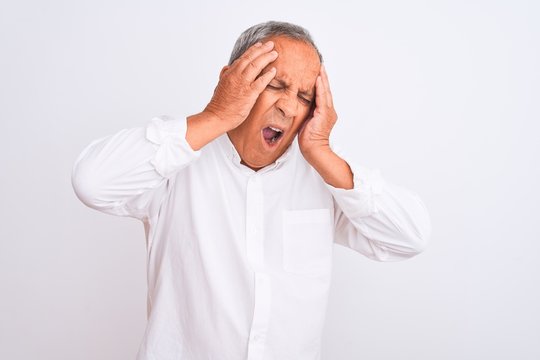 Senior grey-haired man wearing elegant shirt standing over isolated white background with hand on head for pain in head because stress. Suffering migraine.
