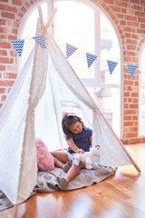 Beautiful toddler girl sitting on the floor playing with unicorn inside tipi at kindergarten © Krakenimages.com