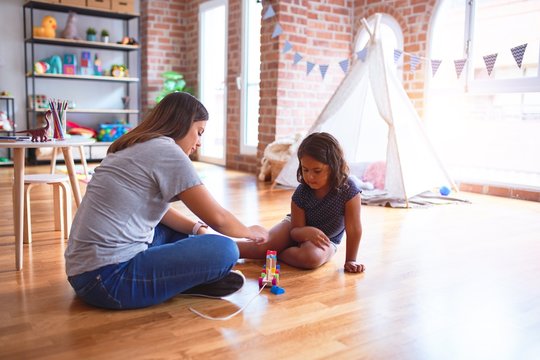 Beautiful teacher and toddler girl playing with train at kindergarten