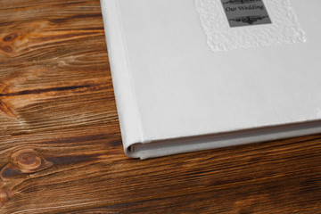 photo book with white   fabric cover. Beige wedding photo album on a wooden background wiht space for text Beige photobook with metal shield photo book with a beautiful stylish cover
