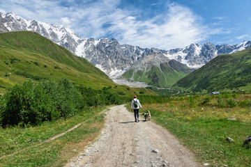 Fototapeta na wymiar Road to Shkar Glacier, river valley in mountains, road along river, group of girl with dog goes in mountains, Ushguli, Caucasus, Georgia