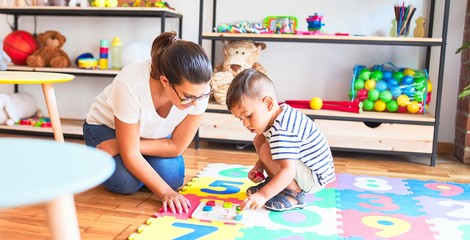 Beautiful teacher and toddler boy sitting on puzzle playing with numbers at kindergarten