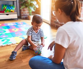 Beautiful teacher and toddler boy sitting eating small chocolate balls at kindergar