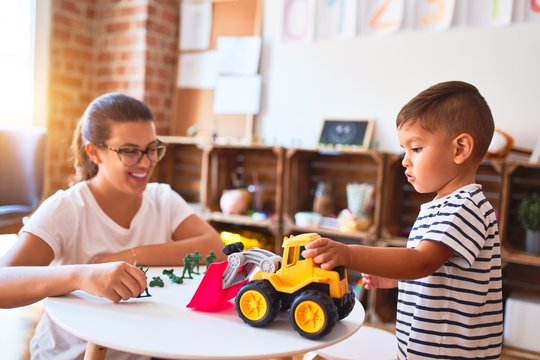 Beautiful teacher and toddler boy playing with tractor and cars at kindergarten