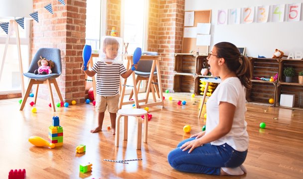 Beautiful teacher and toddler boy playing with plastic basket at kindergarten