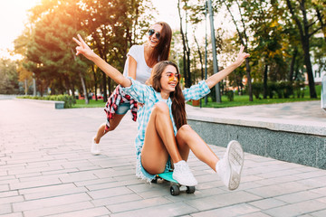 Two stylish excited girls have fun and skateboard in the Park in Sunny weather